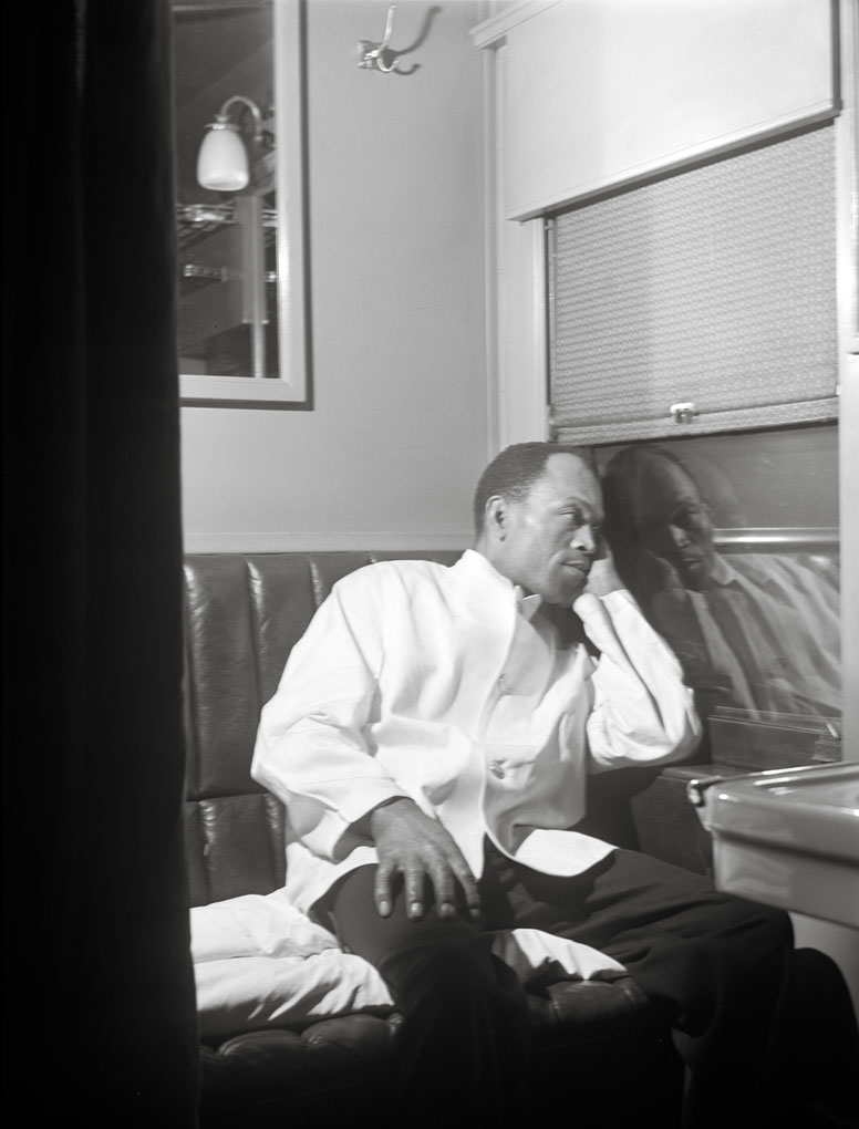 A Pullman Porter in a white uniform jacket, rests aboard a passenger car