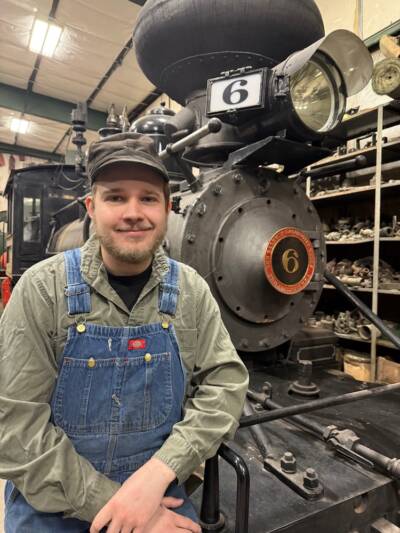 Young individual sitting in front of a narrow gauge steam locomotive
