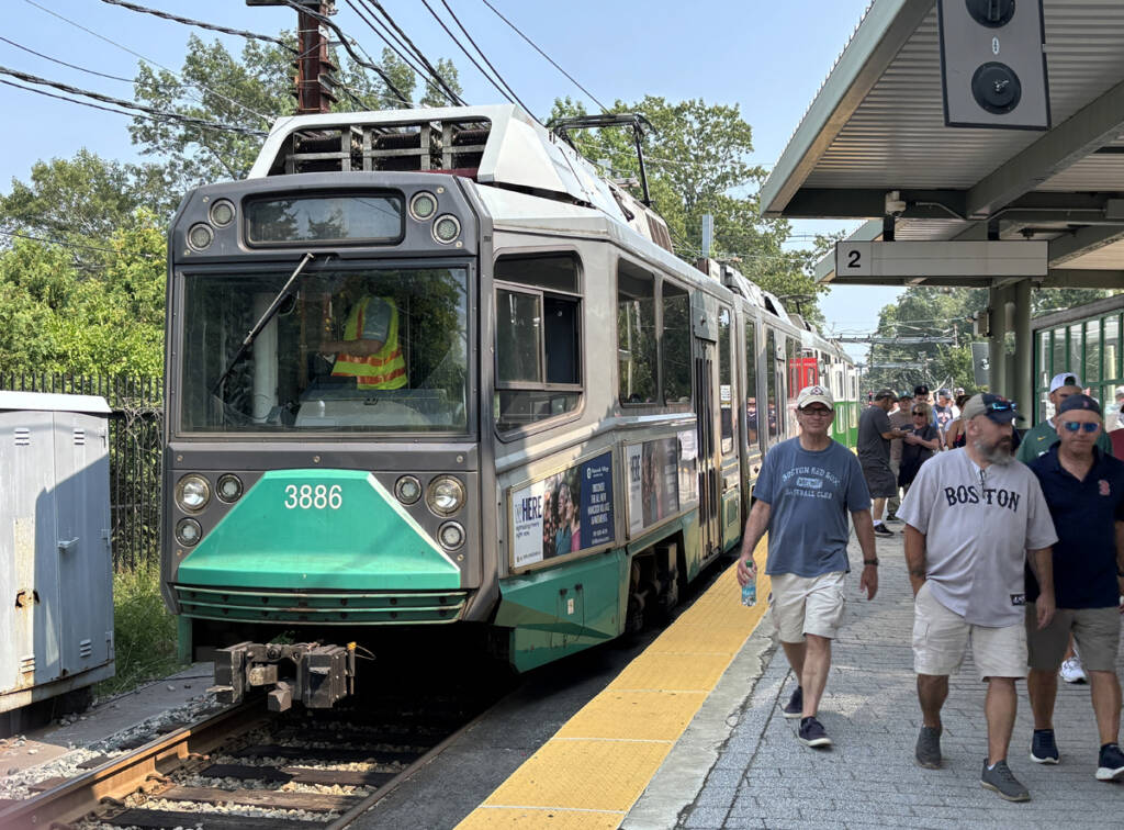 Light rail train, gray with green nose, at station