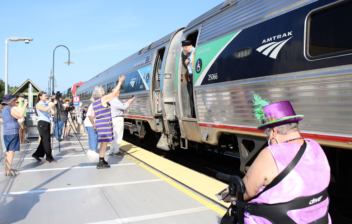 Passenger train departing station with several onlookers on platform
