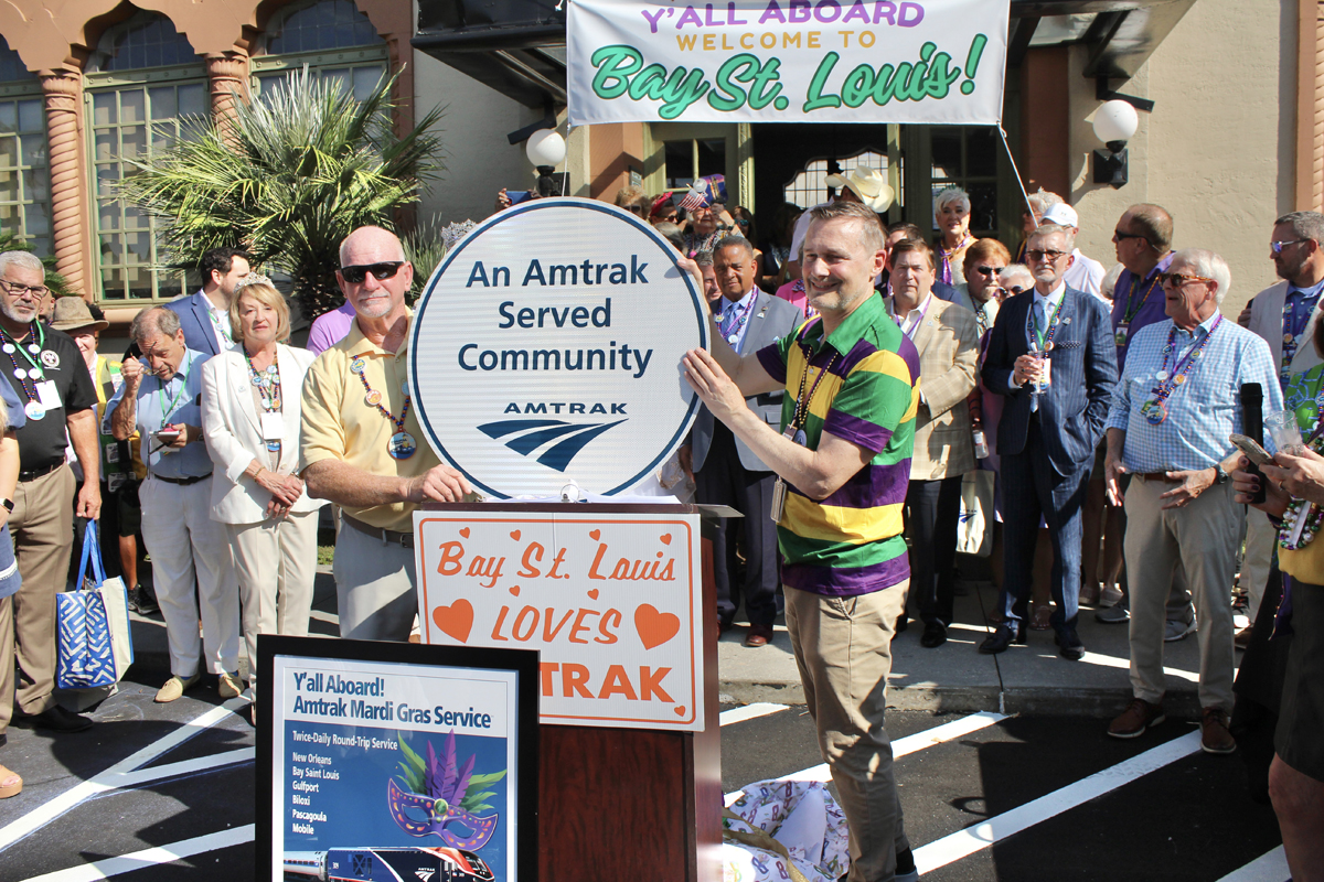 Men holding round sign reading "Amtrak served community" Aug. 16, 2025.