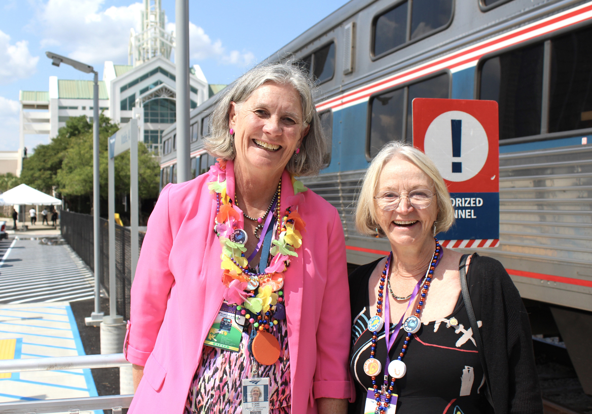 Two smiling women on station platform with train in background. Aug. 16, 2025