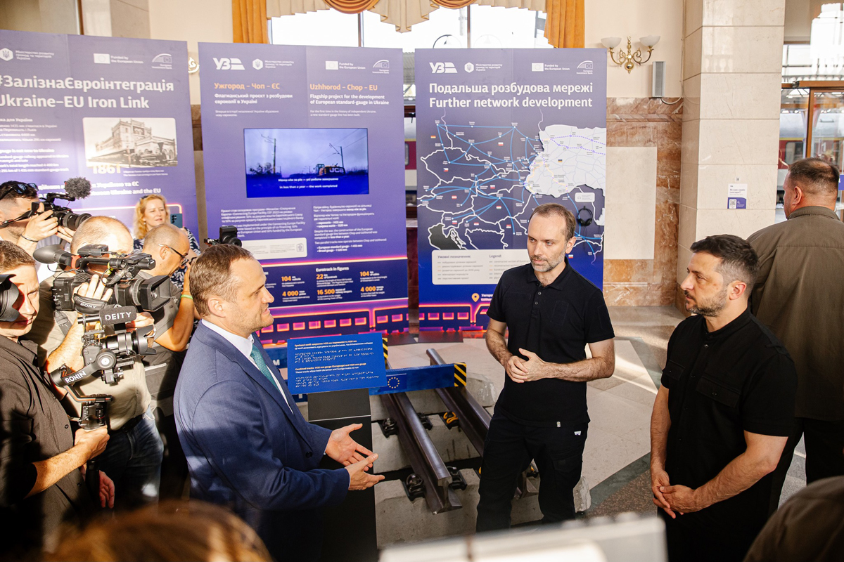 Three men talking in front of displays explaining new Ukraine standard-gauge rail line