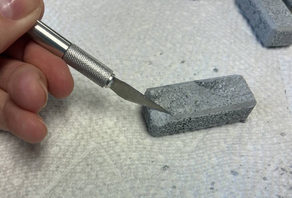 hand holding hobby knife next to small gray block