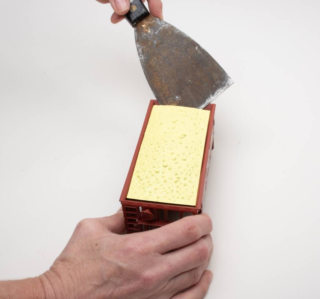 hand holding putty knife near model ore car