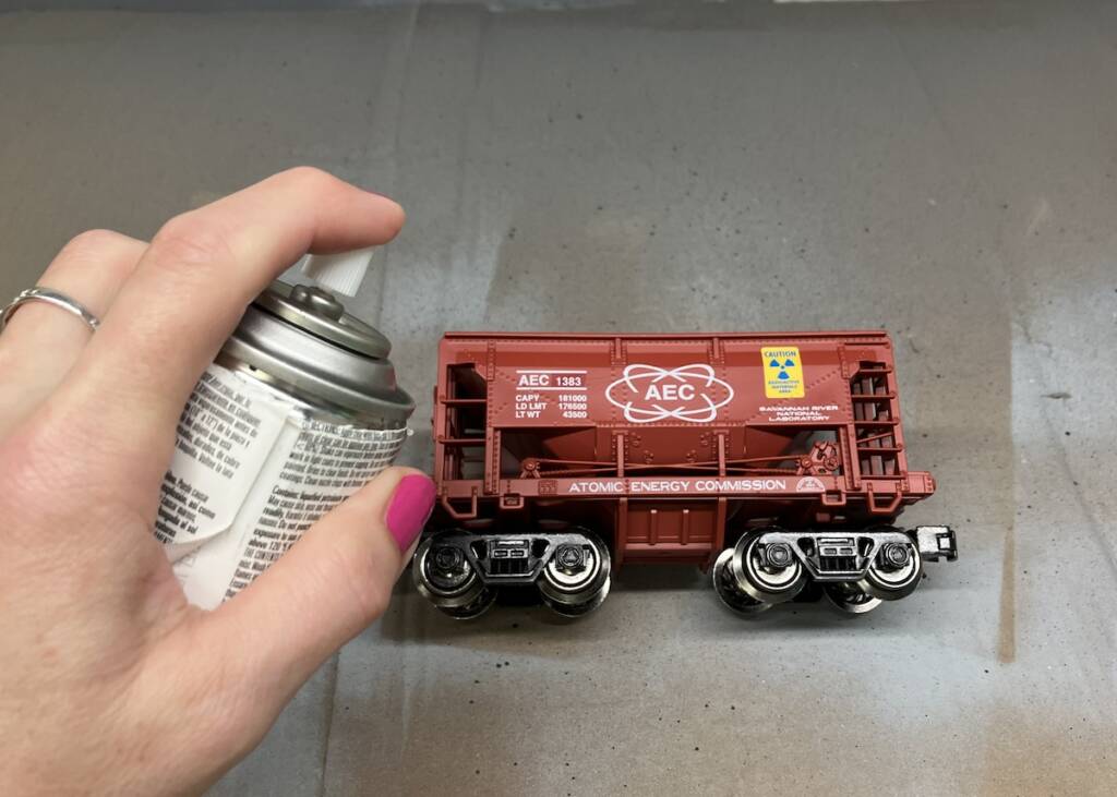 hand holding spray can of paint next to an ore car
