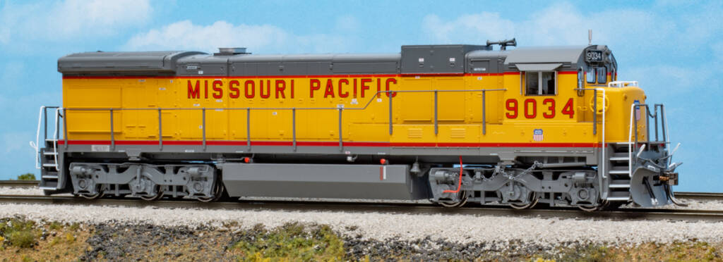 Color photo of HO scale diesel locomotive painted yellow and gray with red, white, and blue graphics on scenicked base with sky backdrop