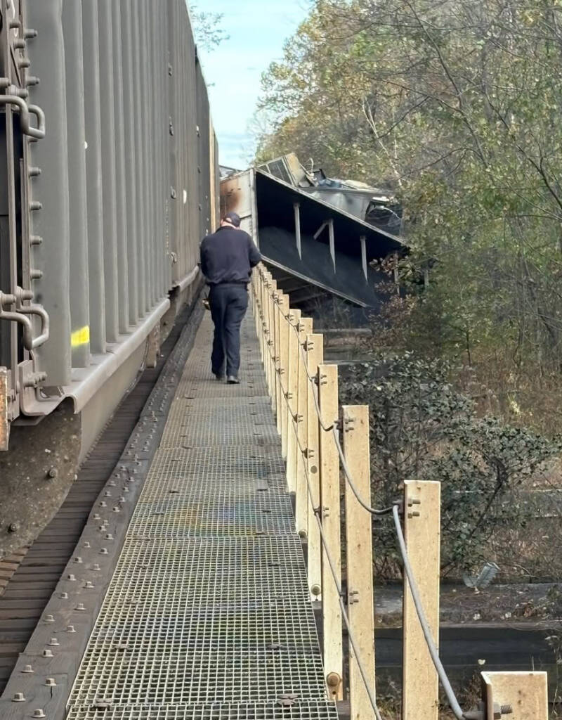 Man walking on railroad bridge with derailed coal hoppers visible in distance