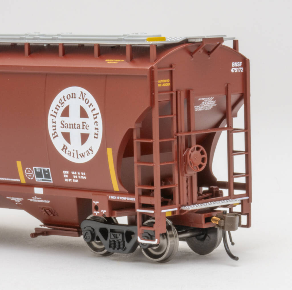 Color photo showing B end of modern three-bay covered hopper painted mineral red with white, yellow, and black graphics on white background.