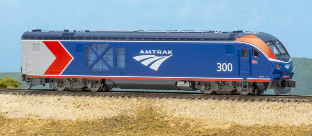 Color photo of modern passenger locomotive painted red, white, blue, and gray with white graphics on scenicked base with a sky blue background. 