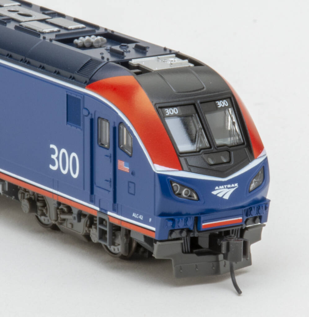Color photo showing nose of streamlined modern passenger diesel painted red, white, gray, and blue with white graphics on white background.