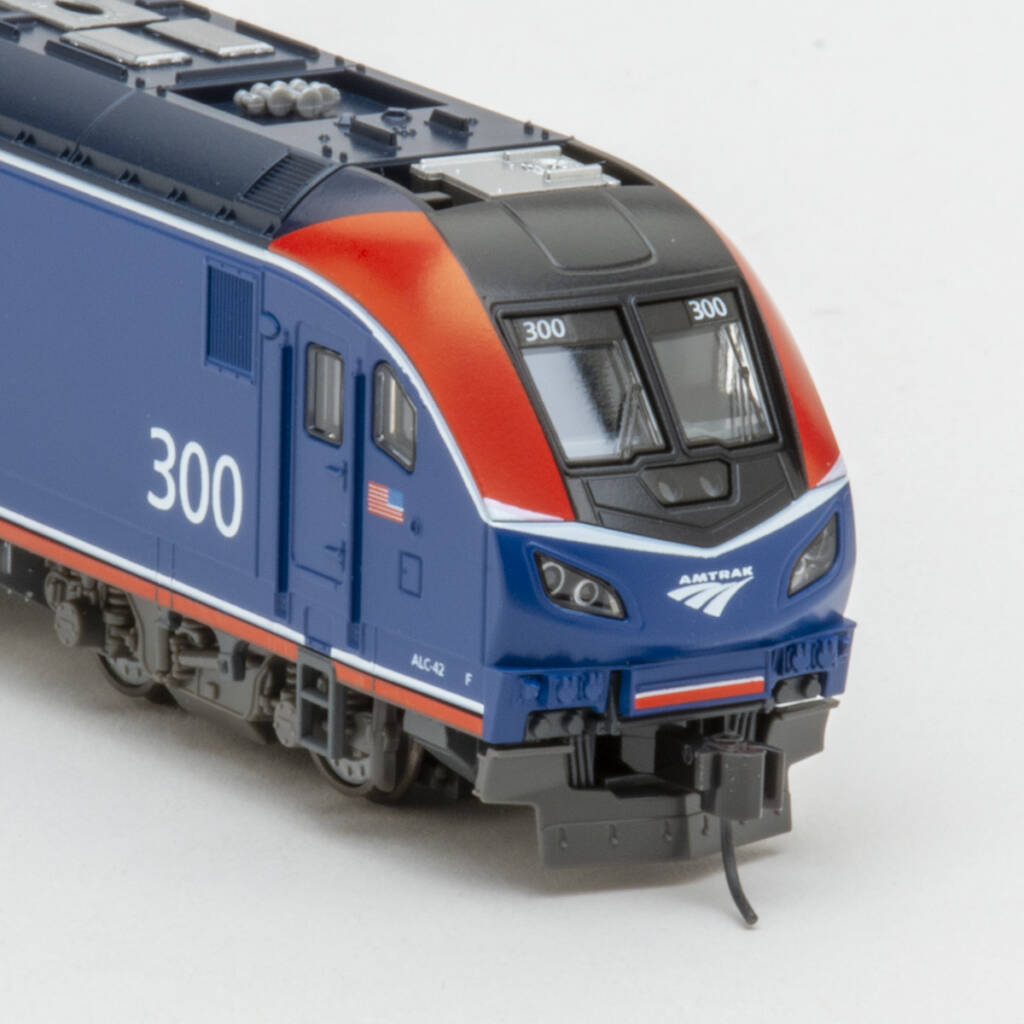 Color photo showing nose of streamlined modern passenger diesel painted red, white, gray, and blue with white graphics on white background.