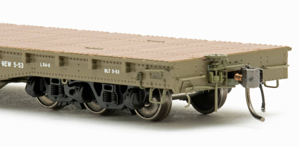 Color photo showing B end of HO scale flatcar painted United States Army Green with white graphics, painted wood deck, and black six-axle trucks with metal wheels on white background.