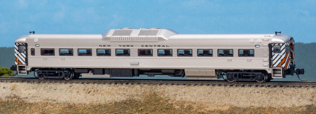 Color photo N scale Budd Rail Diesel Car with stainless steel finish and black, orange, and white stripes on ends on scenicked base with a sky blue backdrop.