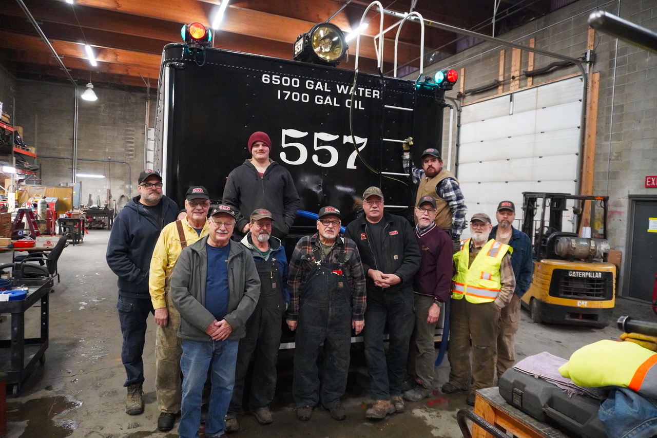 Group of volunteers standing around a steam locomotive tender. Alaska No. 557 fires up after 60 years.
