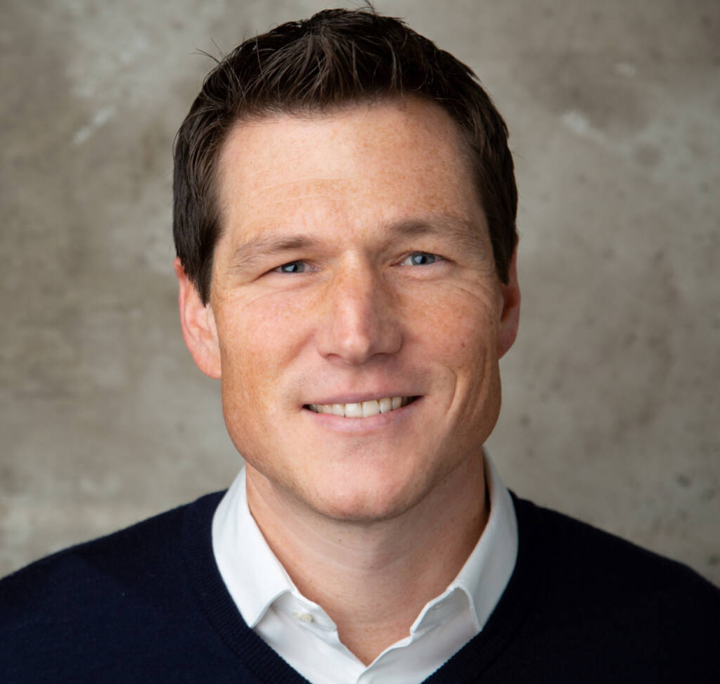 Smiling dark-haired man in black sweater and white shirt