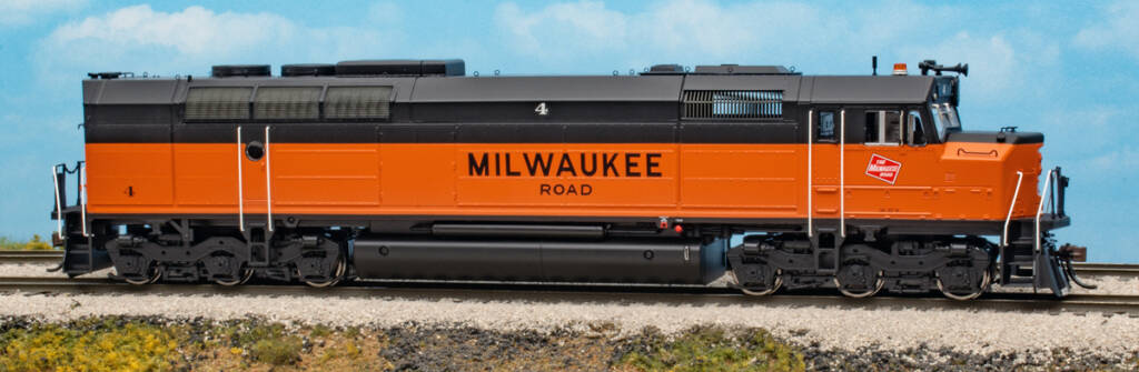 Color photo of HO scale diesel with cowl body painted orange and black on scenicked base with a sky blue background.