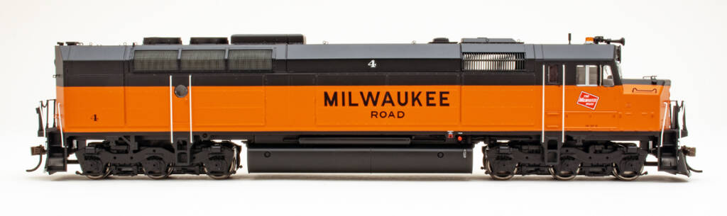 Color photo showing side view of HO scale cowl-body diesel painted orange and black on white background.