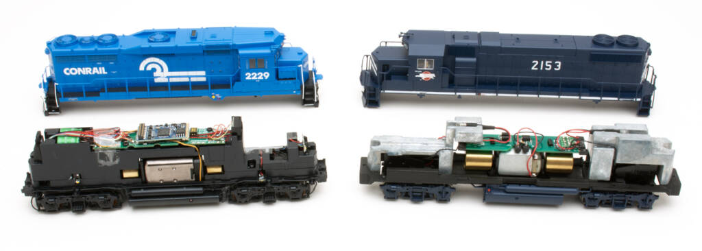 Color photo showing two HO scale locomotive shells, one dark blue and one light blue, with mechanisms in foreground on white background.