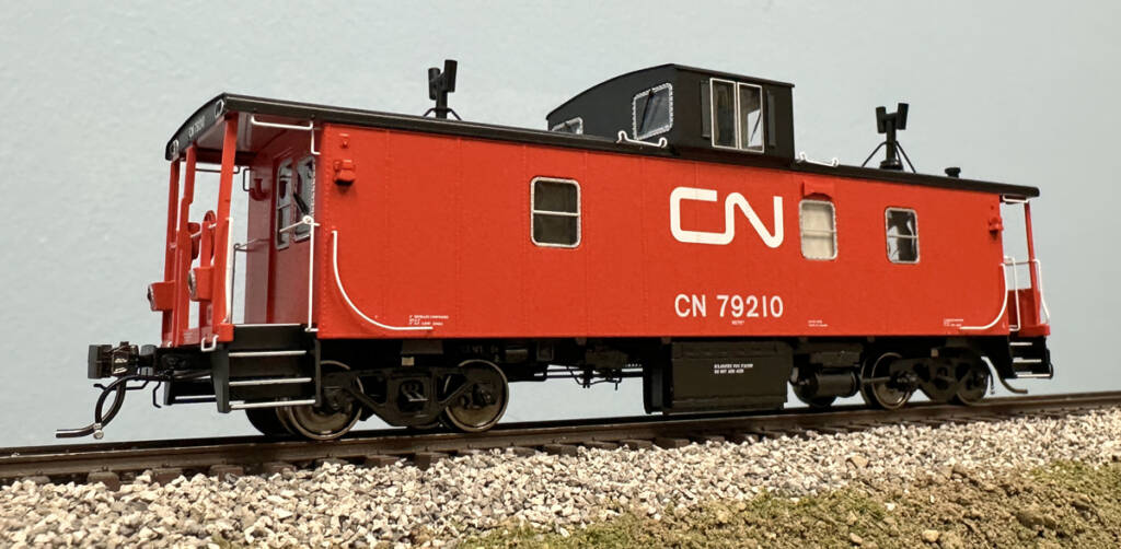 Color photo of HO scale caboose painted red and black with white graphics on scenicked base with a blue backdrop.