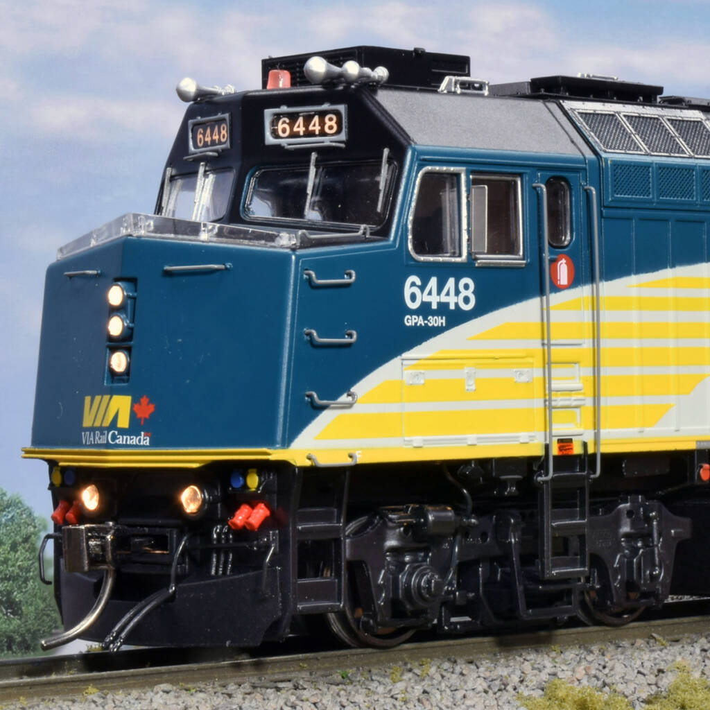 Color photo showing nose of HO passenger locomotive painted black, dark blue, yellow, and gray on scenicked base with a sky background with clouds.