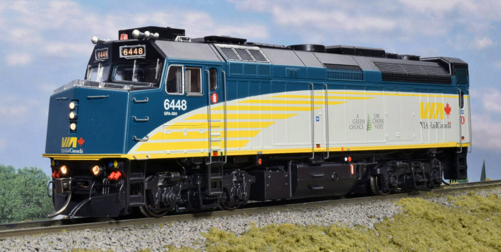 Color photo of HO passenger locomotive painted black, dark blue, yellow, and gray on scenicked base with a sky background with clouds.