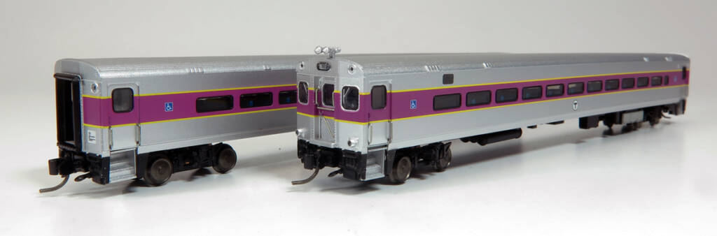 Color photo of two N scale Comet cars painted stainless steel with purple and yellow stripes with black, white, and blue graphics.