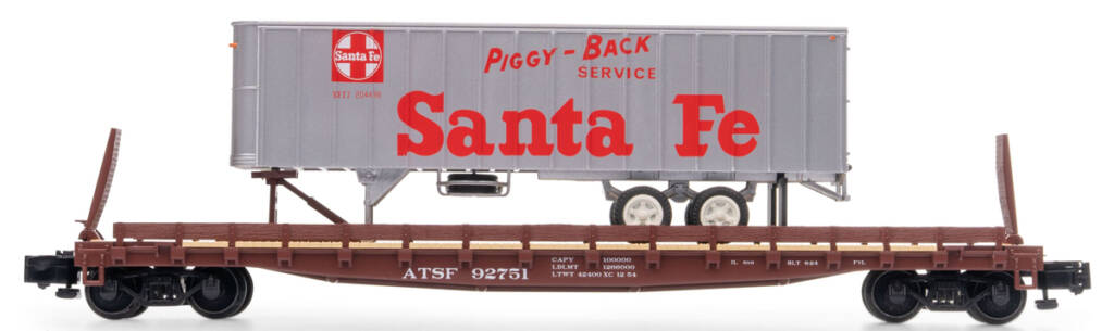 Color photo of S scale flatcar painted brown with white graphics and black solid-bearing trucks with silver trailer painted silver with red and white graphics on white background.