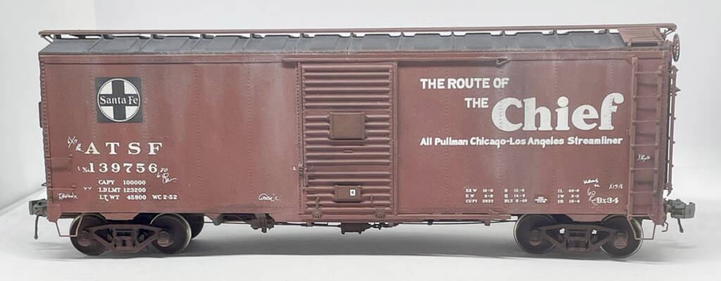Color photo showing HO scale boxcar painted brown and black with black and white graphics on white background.