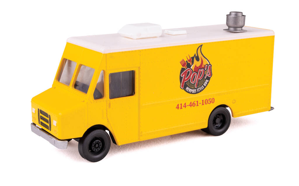 Color photo of delivery truck painted yellow with white roof; red, white, yellow, and black graphics; and rooftop vents on white background.