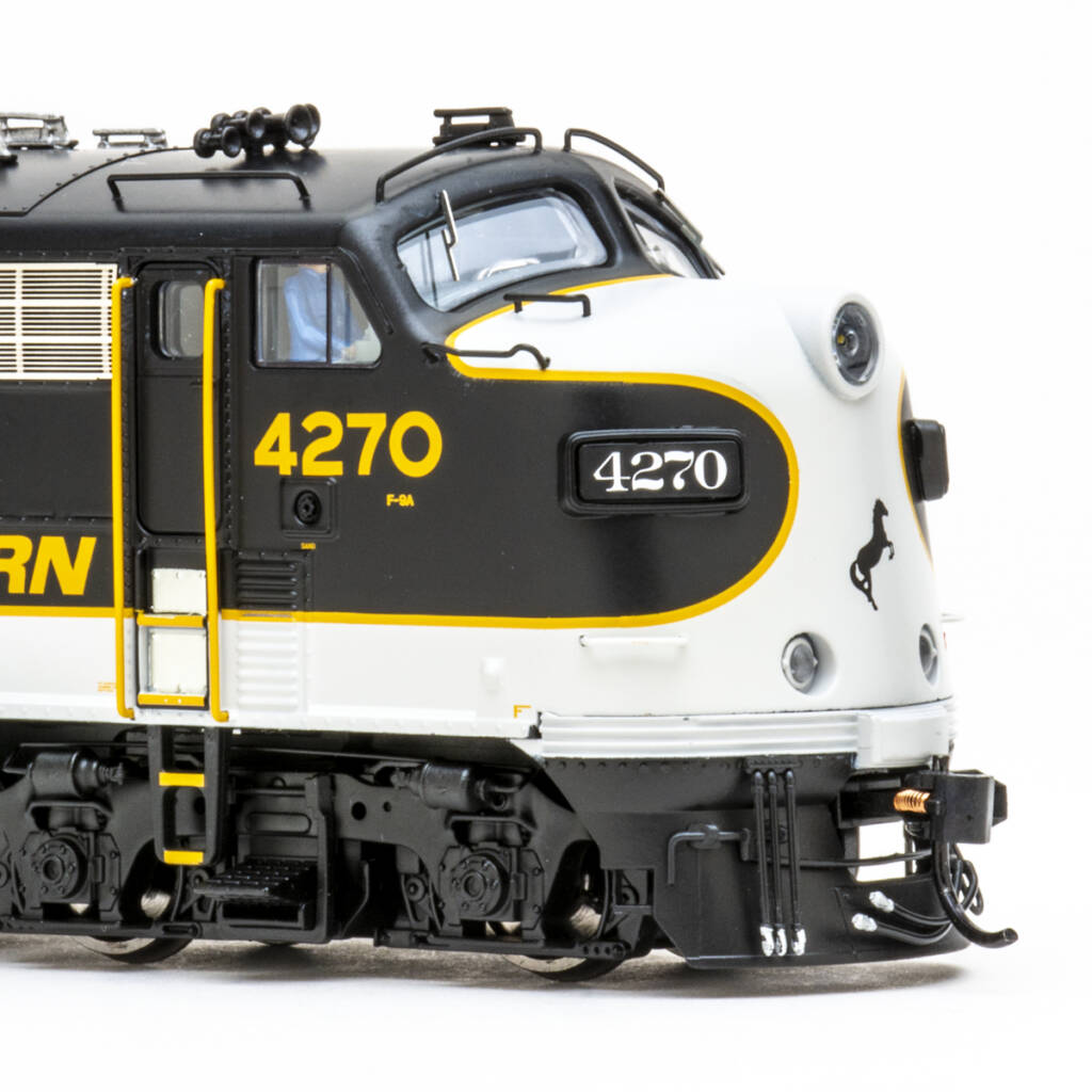 Color photo showing nose of HO scale EMD four-axle cab unit painted black, white, and gold with gold, black, and white graphics on white background.