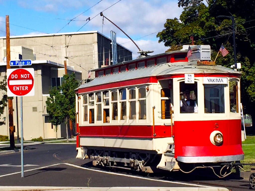 Red and cream-colored trolley car running along city street.