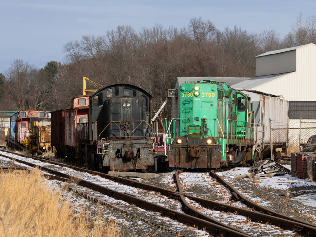 Green locomotive passes black locomotive at small railroad yard
