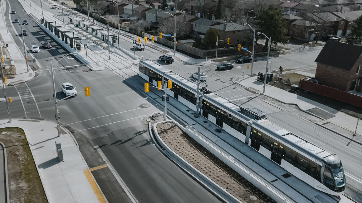 Aerial view of predominantly white, four-car light rail train running in center divider of roadway