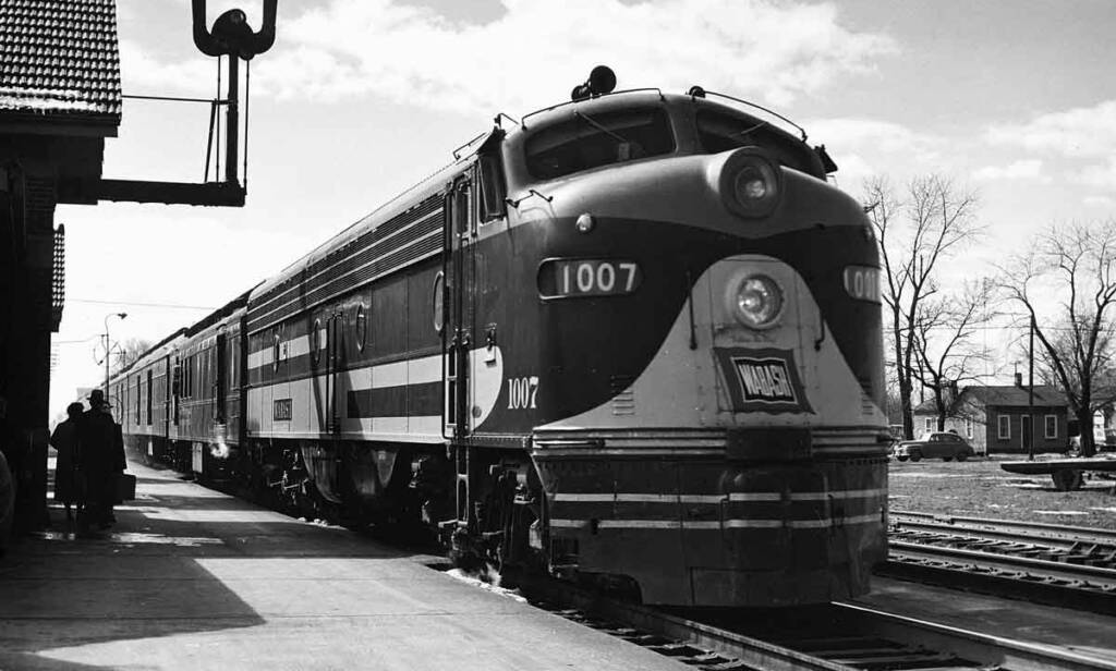 a black and white photograph of a streamlined locomotive next to a passenger station