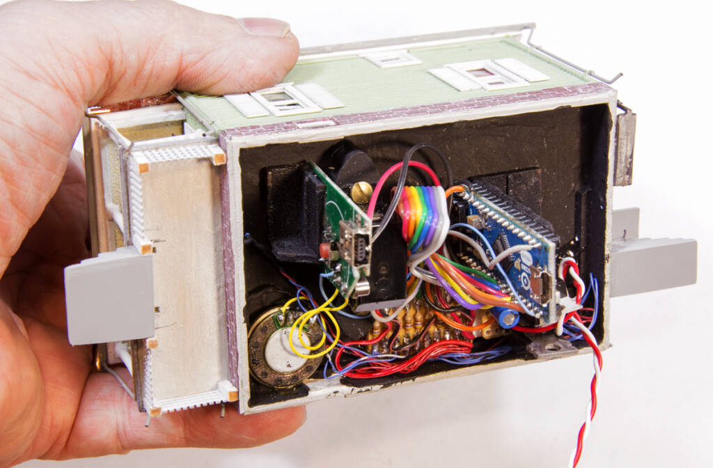 Color photo of hand holding a scale house with wires and printed-circuit boards in the interior.