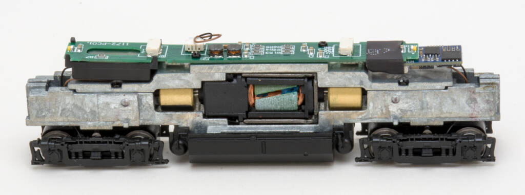 Color photo showing unpainted metal chassis of N scale diesel locomotive with black trucks and fuel tank attached on white background.