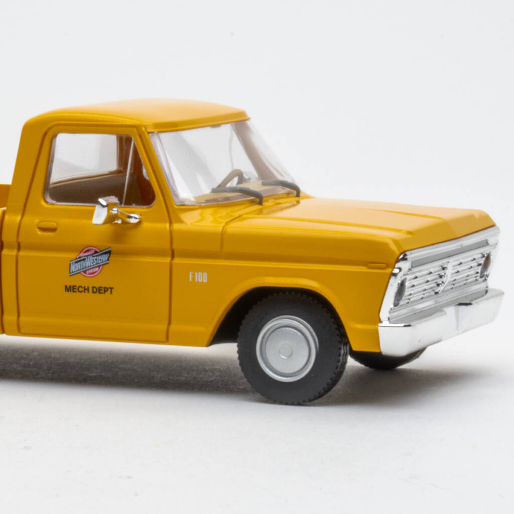 Color photo showing front half of O scale pickup truck painted yellow with red, black, and white graphics and silver wheels on white background.