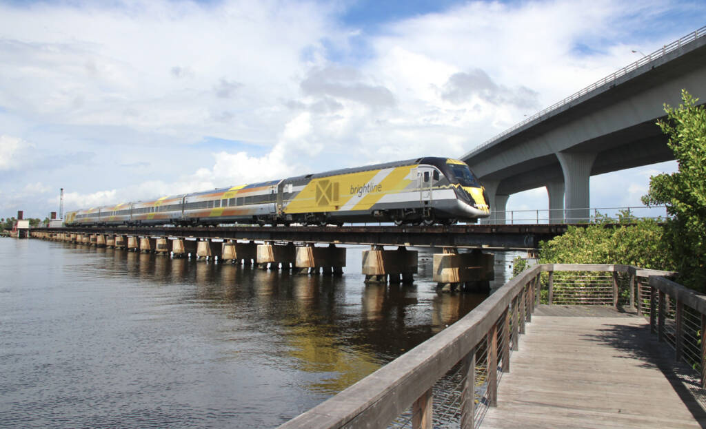 Yellow and white locomotive leads passenger train across bridge