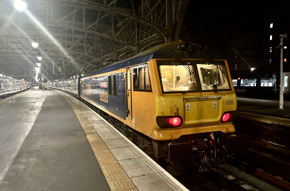 Yellow and blue electric locomotive on passenger train in station trainshed at night