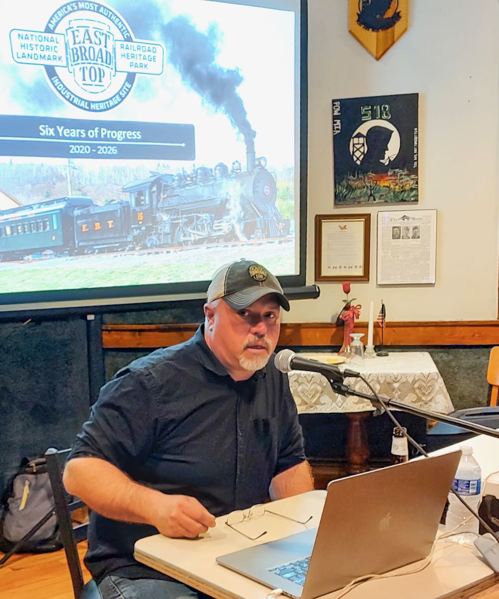 Man speaking with video screen in background
