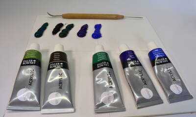five tubes of oil paint, with five blobs of paint and a sculpting tool on a scrap of white matboard
