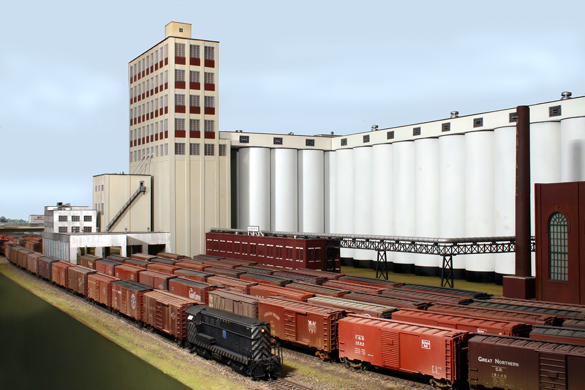Sea of dark red boxcars in front of a very large grain terminal with a tan headhouse and multiple cylindrical concrete grain silos