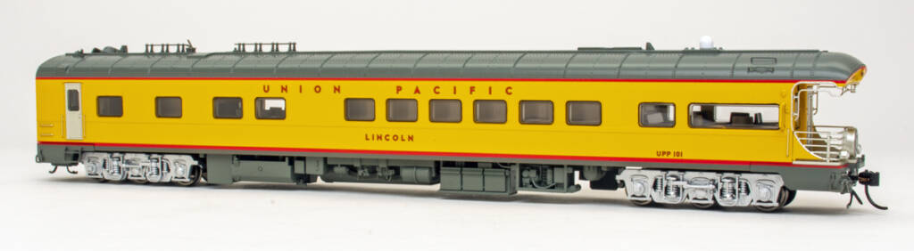 Color photo of HO scale passenger car painted yellow and gray with red stripes and graphics and silver six-wheel trucks on white background.