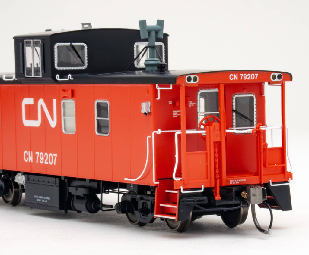 Color photo showing portion of HO scale caboose painted red and black with white graphics on white background.