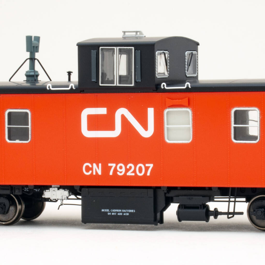 Color photo showing portion of HO scale caboose painted red and black with white graphics on white background.