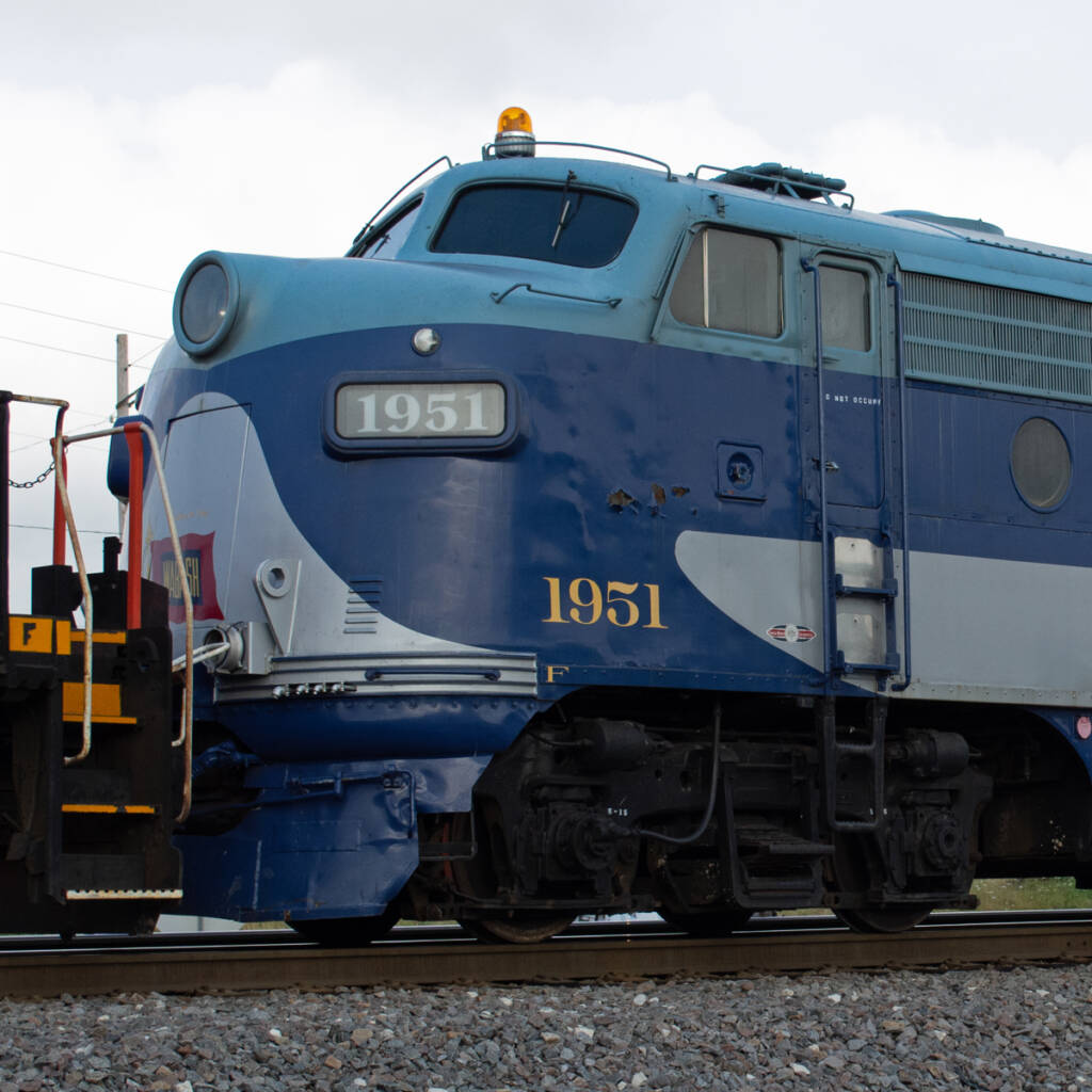 Color photo showing front of EMD four-axle cab unit painted blue and gray with yellow graphics.