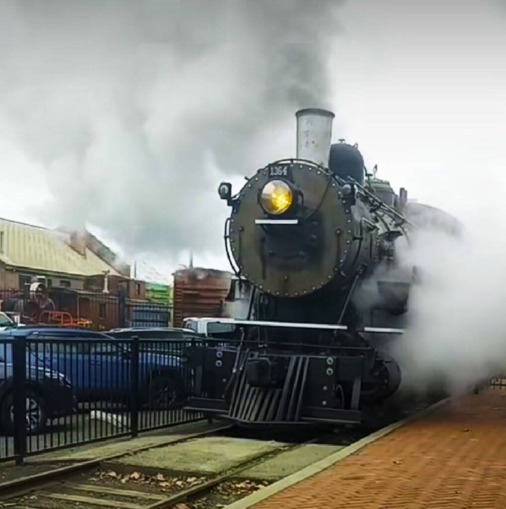 Black steam locomotive with steam and smoke along a station platform. Northern Pacific No. 1364 runs again after 73 years.