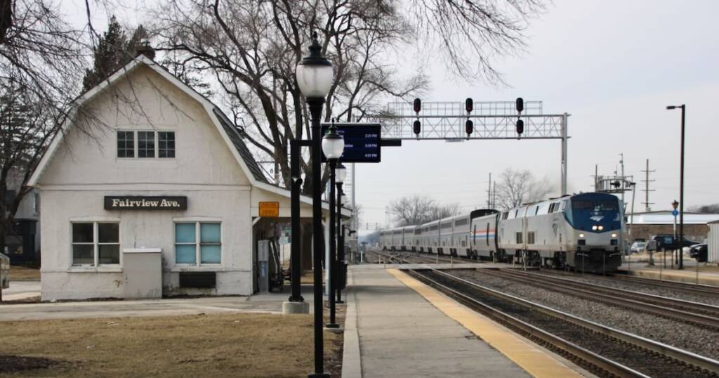 Passenger train passing white, barn-like station
