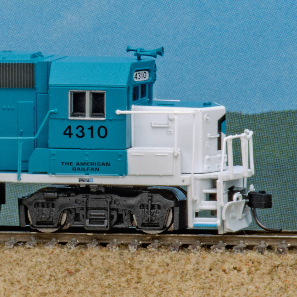 Color photo showing short hood and cab of N scale EMD hood unit painted blue and white with black and white graphics on scenicked base with a sky blue background.